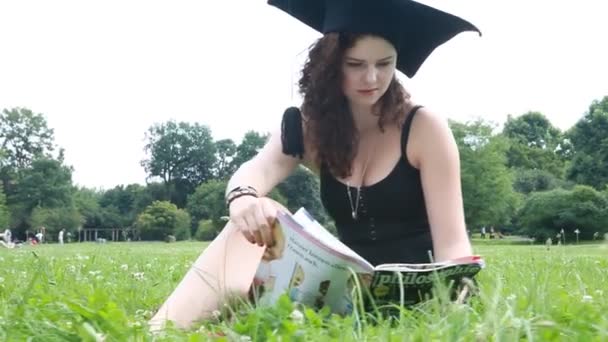 Молодий випускник університету читає в парку — стокове відео