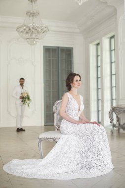 Şık düğün çift damat ve gelin beyaz bir stüdyoda poz. Mutlu çift gülüyor. Beyaz elbise. Beyaz takım. Gençlik. Düğün. Avize. Kanepe. Kapıyı.