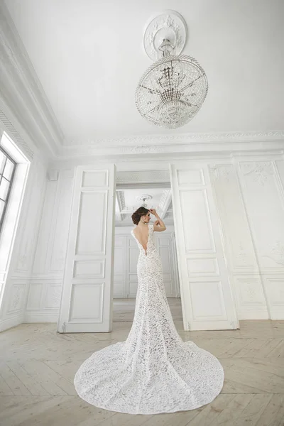 Красивая невеста позирует в свадебном платье в белом фото студии. Зеркало. Диван. Букет. Дверь. Люстра . — стоковое фото