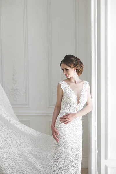Красивая невеста позирует в свадебном платье в белом фото студии. Зеркало. Диван. Букет. Дверь. Люстра . — стоковое фото