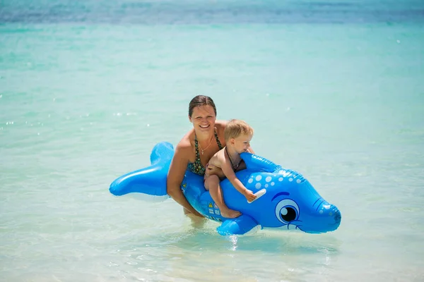Moeder en zoon zwemmen in de oceaan op een opblaasbare dolfijn. — Stockfoto