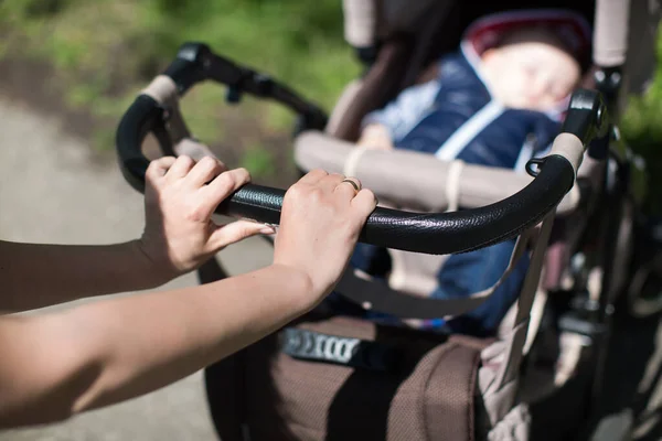 Joven madre caminando y empujando un cochecito en el parque . —  Fotos de Stock