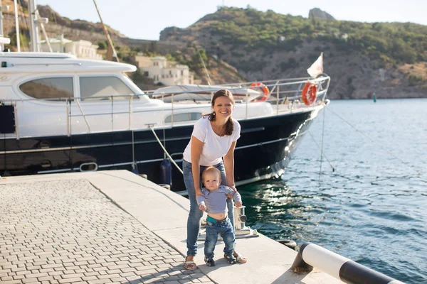 Mooie moeder is wandelen op de pier met haar kleine jongen zoon met eerste stappen. — Stockfoto