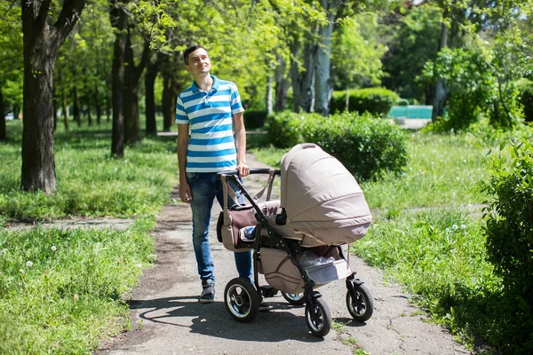 Young man walking in an autumn park with a baby stroller. — Stock Photo, Image