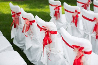 Düğün töreni açık havada. Kırmızı kurdeleli beyaz sandalyeler