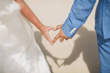 Çok güzel bir gelin ve bir denizin arka planında el ele tutuşan şık bir damat. Gelin ve damat kalp şeklinde el ele tutuşuyorlar..