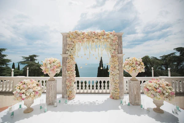 Elegant bröllop båge med färska blommor, vaser på bakgrunden av havet och blå himmel — Stockfoto
