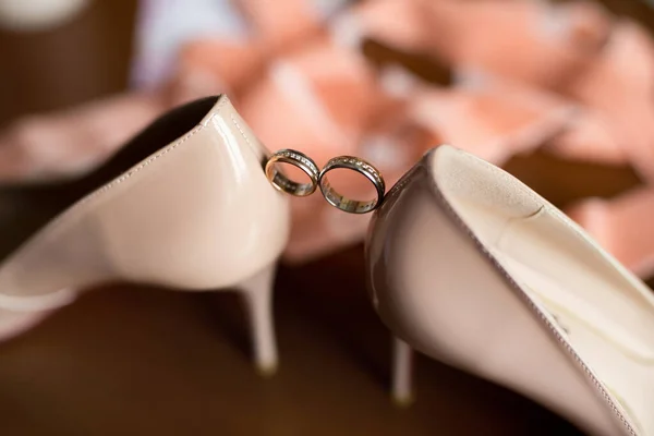 Gold wedding rings between the bride s wedding shoes. — Stock Photo, Image