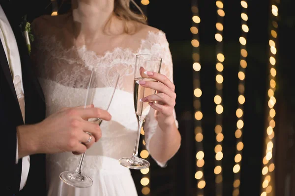 Panna młoda i pan młody trzymają kryształowe kieliszki wypełnione szampanem. — Zdjęcie stockowe