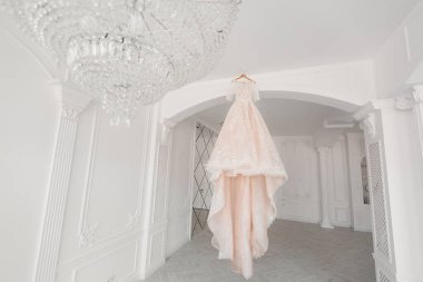 Lüks şeftali rengi gelinlik beyaz bir odada bir avizeye asılı..