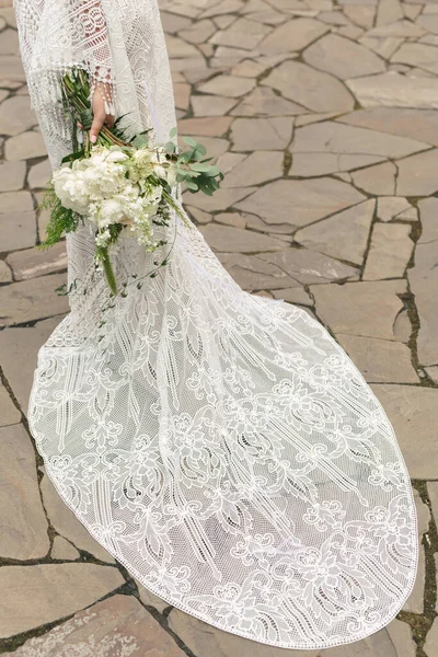 Delicado ramo de peonías blancas en las manos de la novia en el fondo del tren del vestido de novia — Foto de Stock