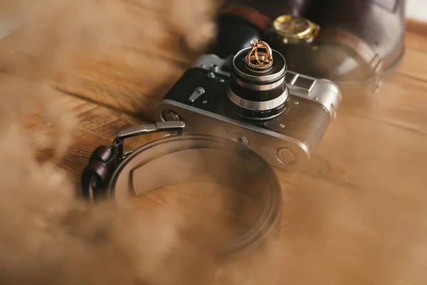 Svatební prsteny na staré kameře, botách, hodinkách a opasku. Mužské atributy na dřevěné podlaze. — Stock fotografie