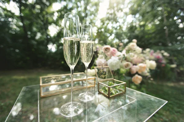Fedi nuziali d'oro in una scatola di vetro, bicchieri di champagne su un tavolo di vetro. — Foto Stock
