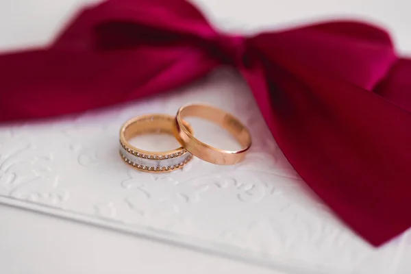 Gold wedding rings on a white card with a red bow. — Stock Photo, Image