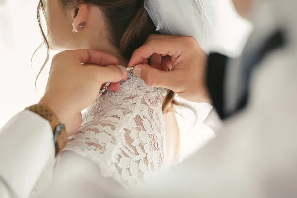 Mains féminines bouton de la robe de mariée à la mariée avec une belle coiffure . — Photo