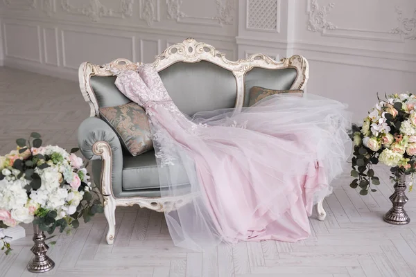 Luxusní růžové svatební šaty leží na šedé pohovce v bílém pokoji. — Stock fotografie