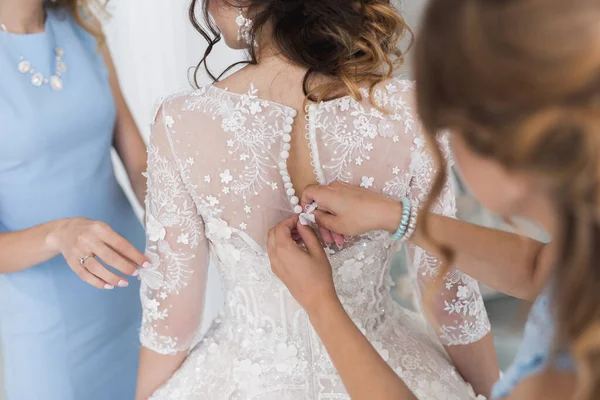 Mains féminines bouton de la robe de mariée à la mariée avec une belle coiffure . — Photo