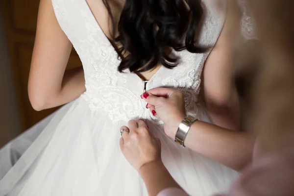 Vrouwelijke handen knop de trouwjurk aan de bruid met een mooi kapsel. — Stockfoto