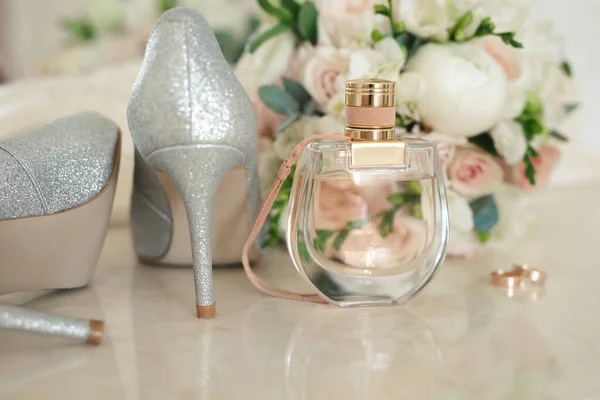 Серебряная обувь невесты, парфюмерия, букет и обручальные кольца на туалетном столике возле зеркала. — стоковое фото