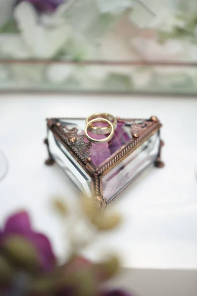 Wedding rings in a glass box with lilac rose petals. — Stock Photo, Image