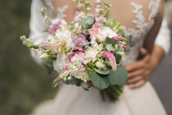 Ženich v bílé košili s kyticí květin v rukou objímá nevěstu — Stock fotografie