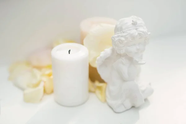 Standbeeld van een engel, een kaars en rozenblaadjes op tafel — Stockfoto