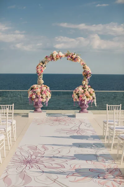 Bruiloft boog met verse bloemen op een zee-achtergrond. Vazen met verse bloemen — Stockfoto