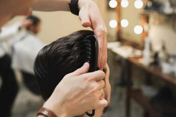 Cabeleireiro masculino profissional faz penteado para homem barbudo na barbearia, visão traseira, barbeiros mão com clipper — Fotografia de Stock