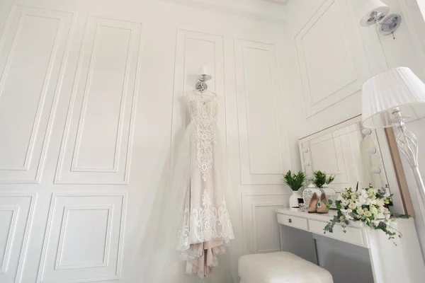 Elegantní svatební bílé šaty visí na zdi během přípravy svatby. Nevěsty ráno. Před ceremoniálem. — Stock fotografie