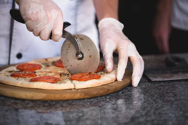 Der Koch schneidet mit einem runden Messer Pizza — Stockfoto