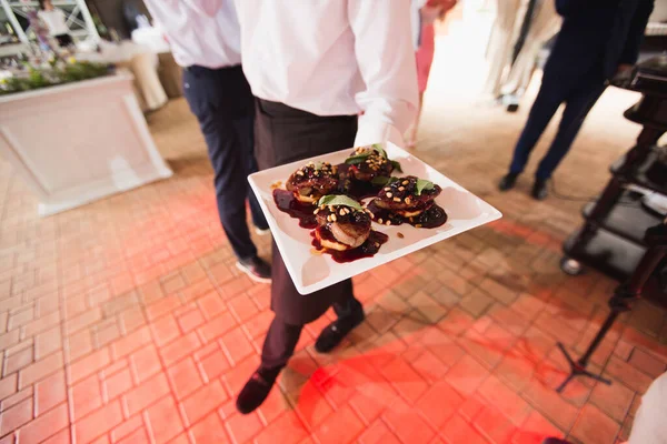 Foie gras s omáčkou, bylinkami a ořechy na talíři v rukou číšníka — Stock fotografie