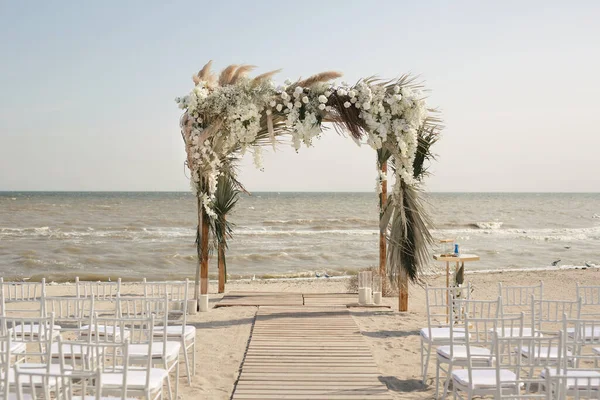 Uteplats för strandceremonier med havsutsikt, vita stolar, blomsterbåge en solig dag. — Stockfoto