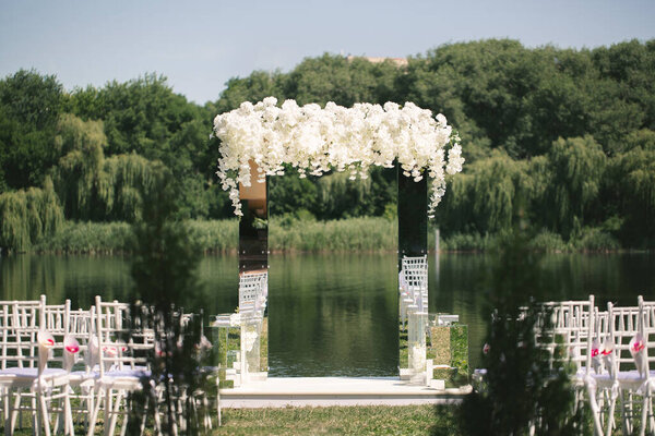 White mirrored wedding arch decorated with white flowers. The concept of an outdoor wedding ceremony venue
