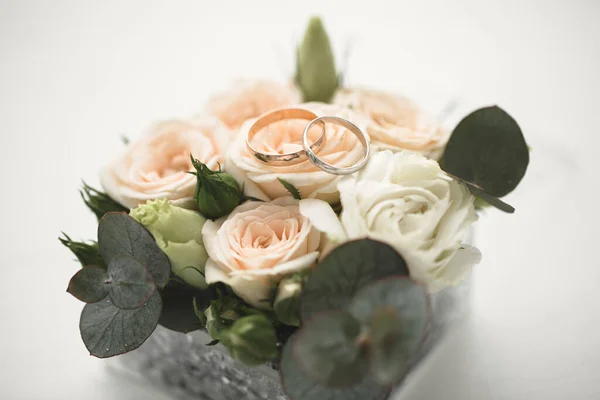 Los anillos de boda de los novios hechos de oro amarillo se encuentran en una rosa rosa. La flor se encuentra en una caja de vidrio con un corte de cobre — Foto de Stock