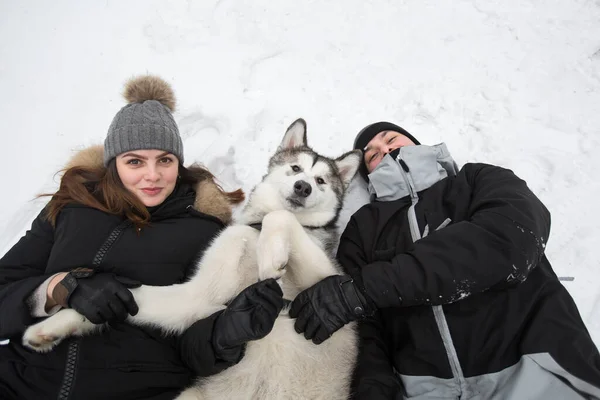Bela família, um homem e uma menina na floresta de inverno com cão. Brincar com o cão Siberian husky — Fotografia de Stock