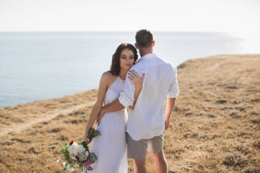 Dağın yamacında duran genç ve güzel bir çift. Beyaz cüppeli insanlar