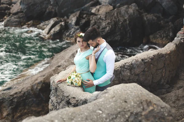 A noiva e o noivo na natureza nas montanhas perto da água. Terno e vestido Tiffany cor. Beijo e abraço — Fotografia de Stock