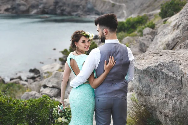 A noiva e o noivo na natureza nas montanhas perto da água. Terno e vestido Tiffany cor. Caminhe de mãos dadas — Fotografia de Stock