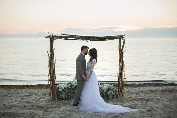 Gelin ve damat sahilde kemer altında. Gün batımı, alacakaranlık — Stok fotoğraf