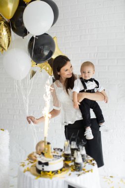 Anne ve oğul birlikte 1. doğum gününü kutluyorlar. Balonlarla gülüp gülüyorlar. Çikolata gibi.