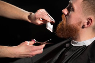 Usta berber dükkanında saç ve sakal kesiyor. Kuaför, makas ve metal tarak kullanarak saç stili yapıyor.