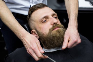 Usta berber dükkanında saç ve sakal kesiyor. Kuaför, makas ve metal tarak kullanarak saç stili yapıyor.