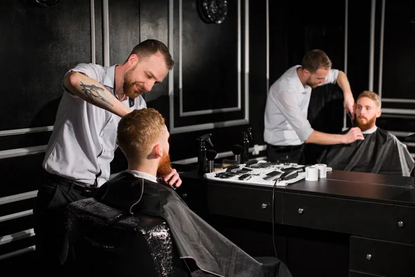 理髪師は理髪店で髪とひげを切ります。美容師ははさみと金属櫛を使用してヘアスタイルを作る — ストック写真