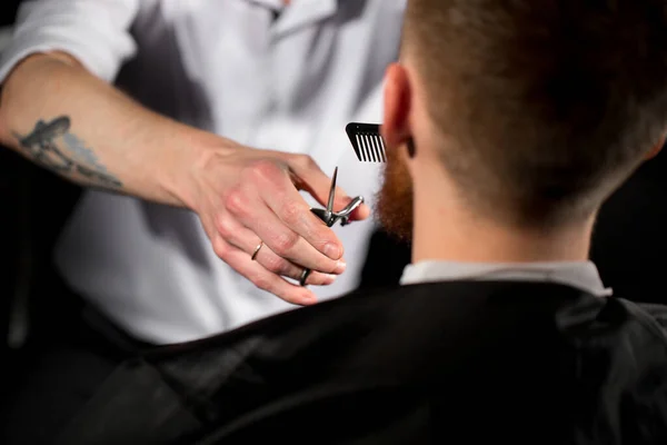 Master taglia capelli e barba nel negozio di barbiere. Il parrucchiere fa l'acconciatura usando forbici e un pettine in metallo — Foto Stock