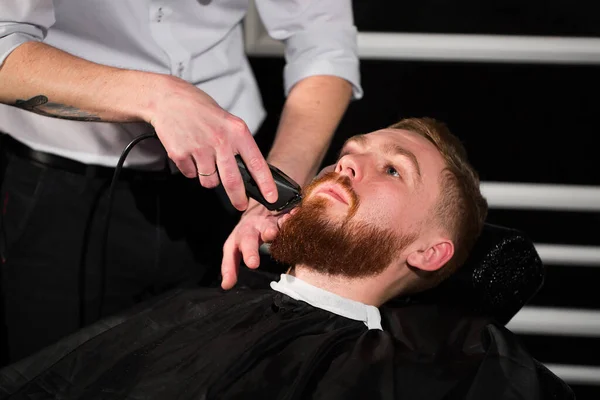 Kuaför, erkek sakalını bıçakla tıraş ediyor. Yakışıklı sakallı adam berber dükkanında kuaför tarafından tıraş ediliyor.. — Stok fotoğraf