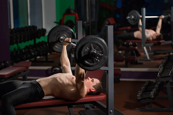 Brutal athletic man pumping up muscles on bench press. — Stock Photo, Image