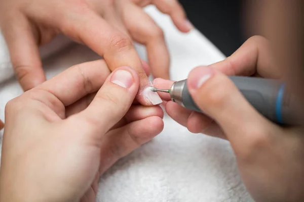 Mistrz używa maszyny elektrycznej do usuwania lakieru do paznokci podczas manicure w salonie. Manicure sprzętowy. Pojęcie pielęgnacji ciała. — Zdjęcie stockowe