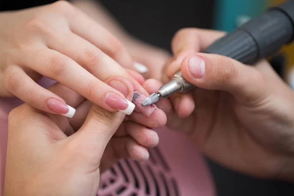 Ujęcie zbliżeniowe mistrza wykorzystuje elektryczną maszynę do usuwania lakieru do paznokci podczas manicure w salonie. Manicure sprzętowy. Pojęcie pielęgnacji ciała. — Zdjęcie stockowe