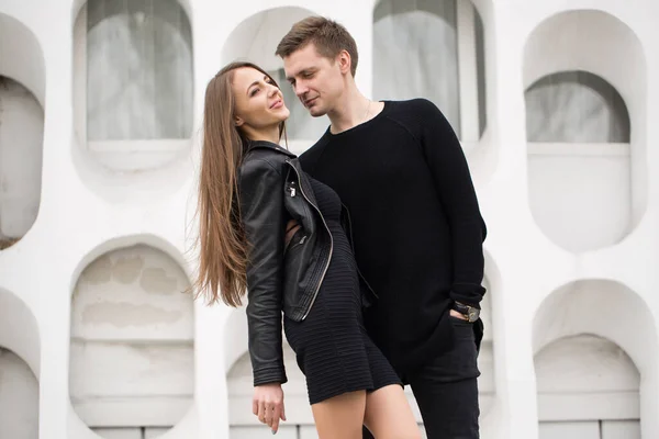 Jovem casal sexy em roupas pretas posando com um fundo na parede branca . — Fotografia de Stock
