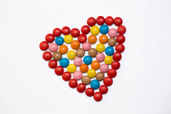 Botões coloridos doces de chocolate na forma de amor no fundo branco . — Fotografia de Stock